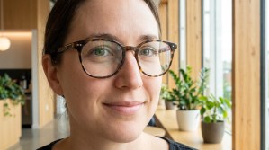 Femme souriante portant des lunettes à monture écailles dans un intérieur lumineux et végétalisé.